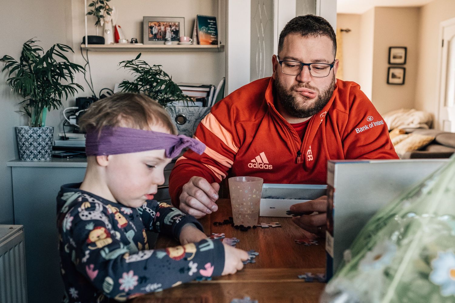 Two people working together at wooden table with plants in background.