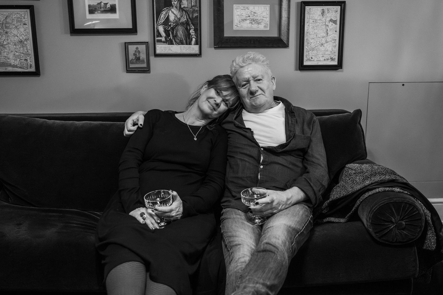 Two people relaxing together on a couch with drinks in a room decorated with framed artwork.