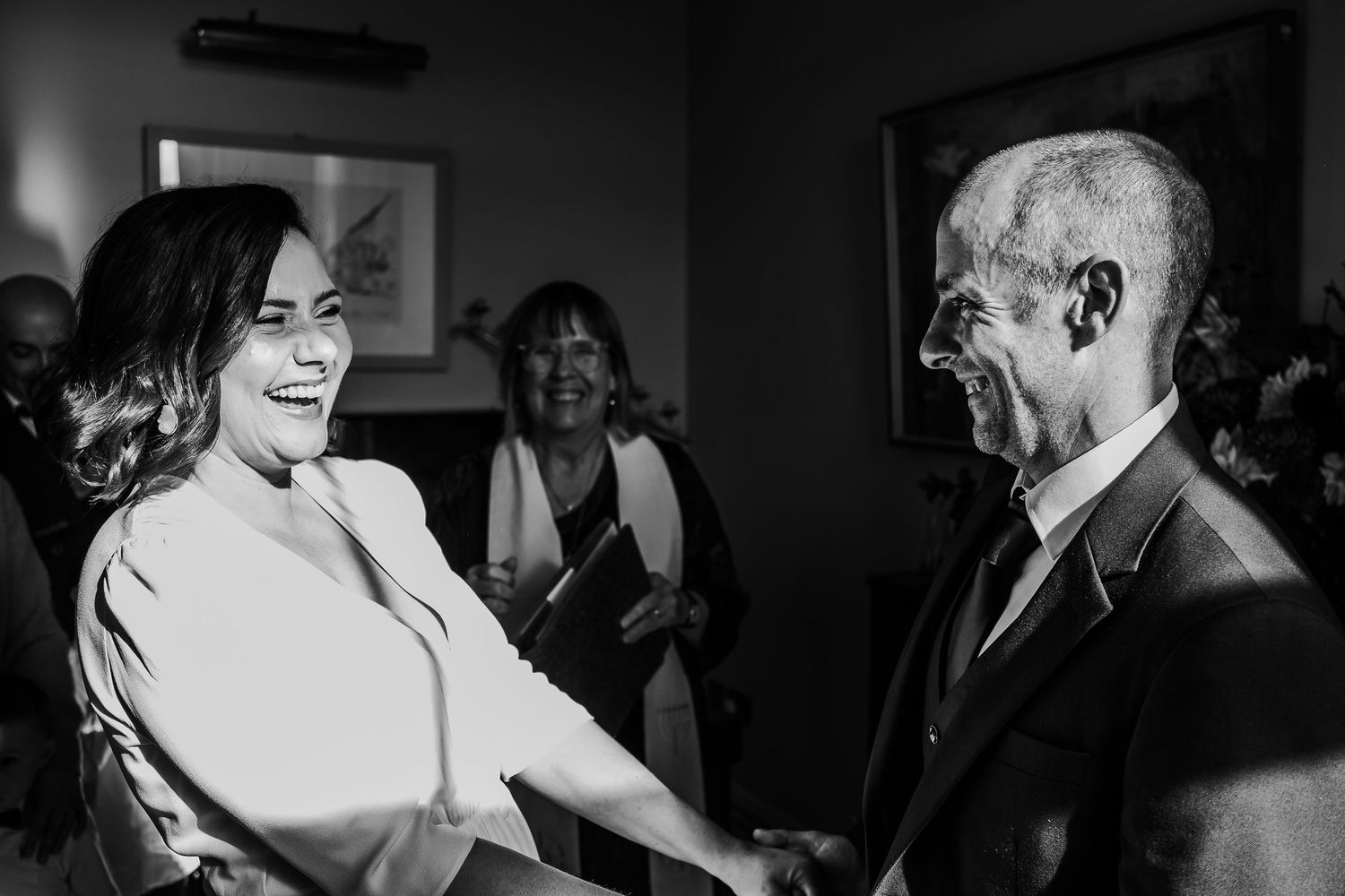 Bride laughs joyfully while shaking hands with elderly guest in black and white wedding reception photo.