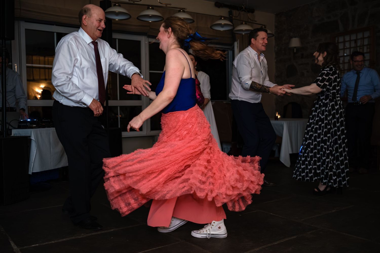 Guests dancing energetically at a wedding reception, woman in pink ruffled dress twirling on the dance floor.