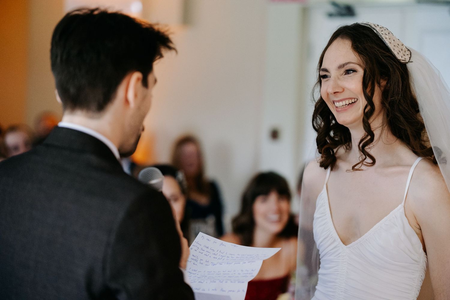 A wedding ceremony exchange of vows between a couple, with the bride wearing a white spaghetti strap dress.