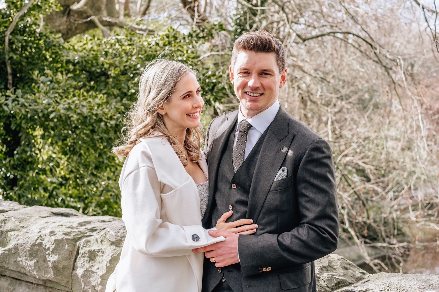 Wedding couple posing together against a stone wall with greenery in the background.