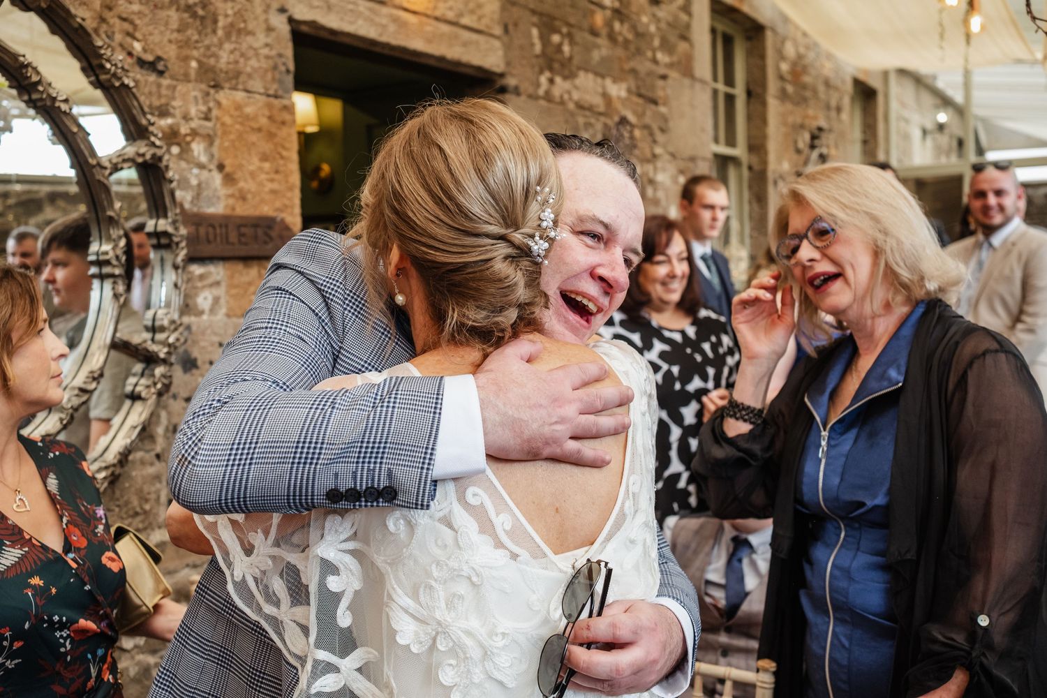 An emotional embrace during an outdoor wedding celebration near a stone building.