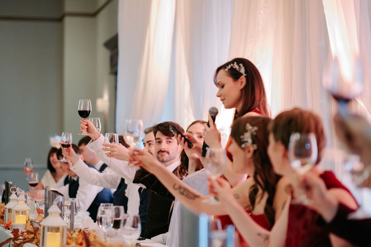 Wedding reception guests raising glasses in celebration at decorated banquet hall.