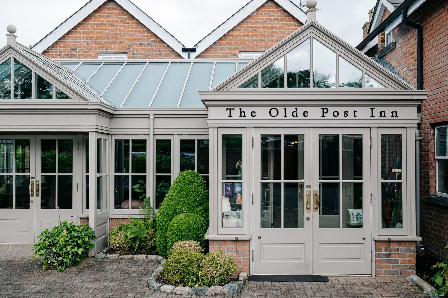 Exterior view of The Olde Post Inn featuring elegant glass conservatory entrance with cream painted doors and brick facade.