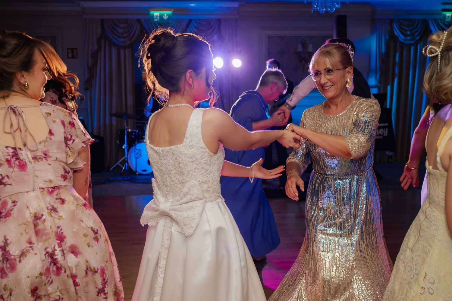 Bride in white gown dancing with a woman in silver dress at a wedding reception with live band.
