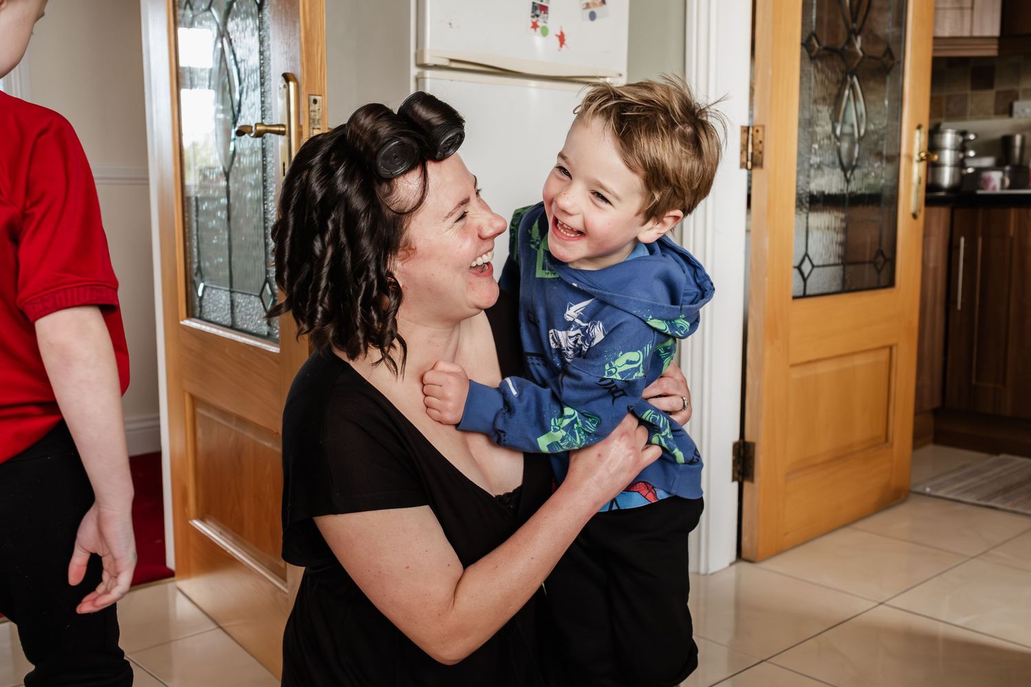 A woman holds a laughing toddler boy in a home kitchen, sharing a joyful moment together.