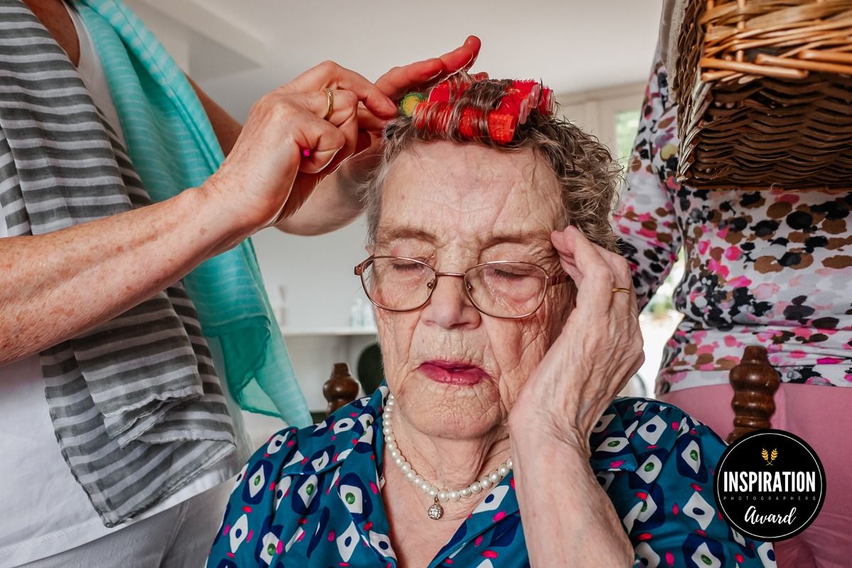 Hands applying red hair curlers while person rests face on hand.