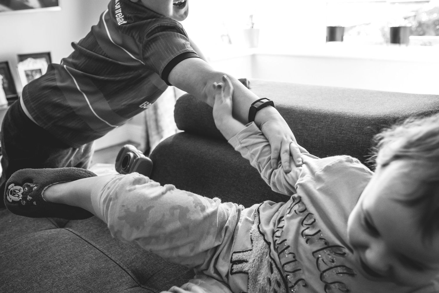 Black and white image of someone helping with leg stretches on a couch.