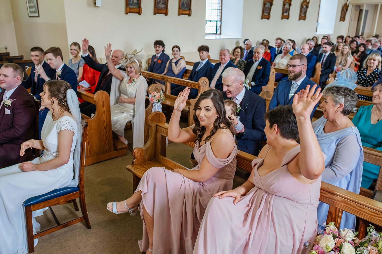 Wedding guests react emotionally during a ceremony in a chapel with stained glass windows and wooden pews.