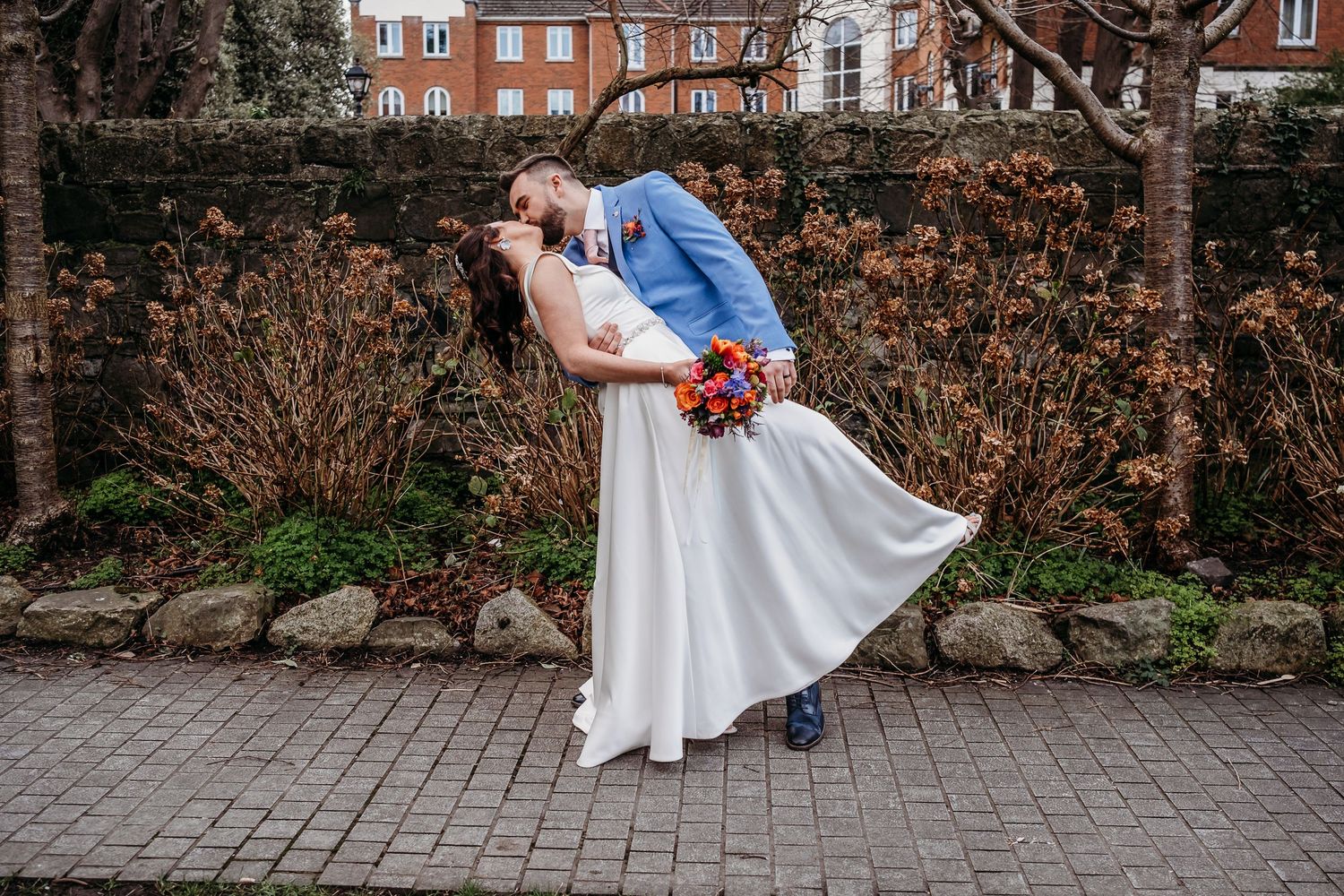 Romantic dip pose on brick pathway with autumn foliage in background.