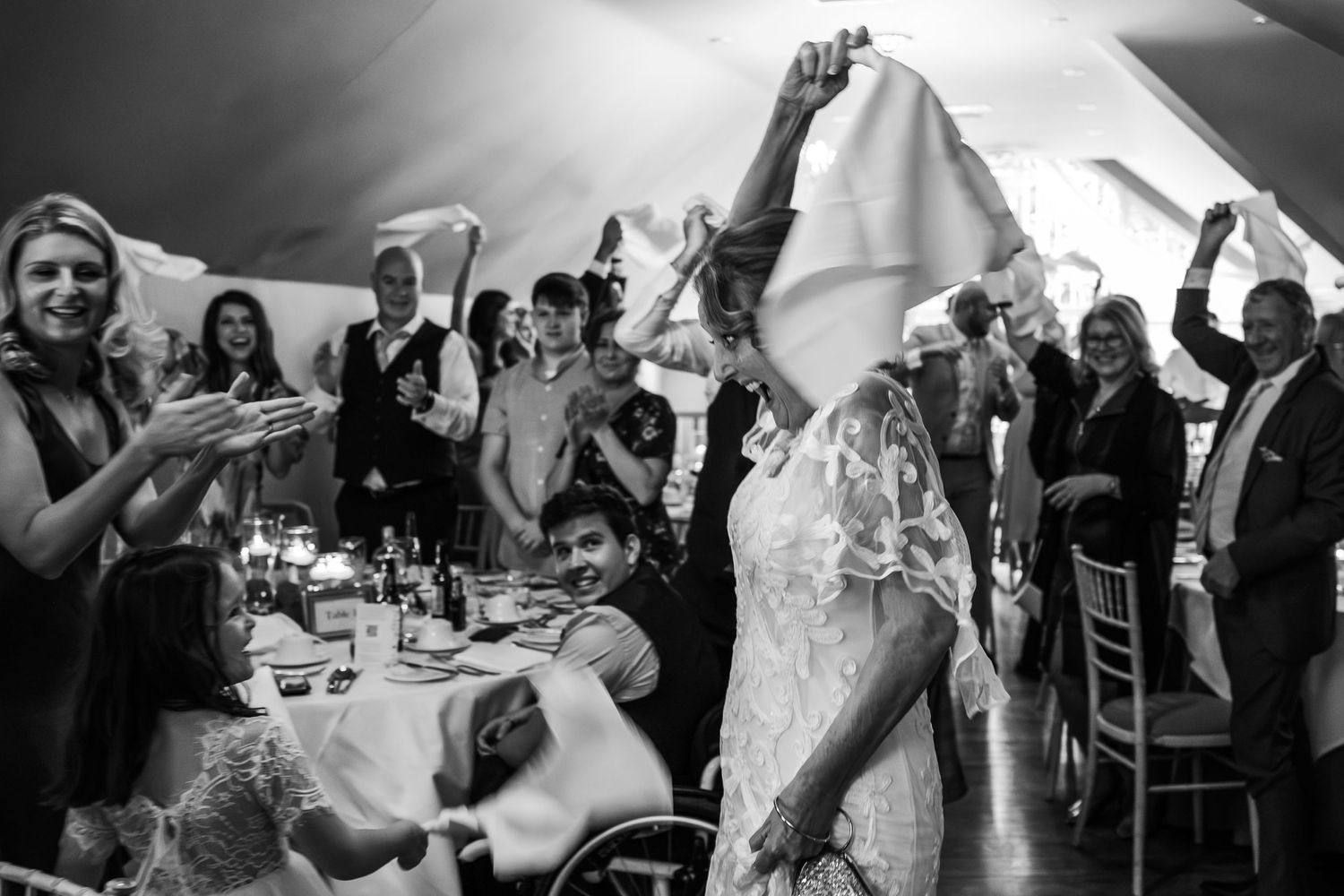 A black and white photo of wedding guests applauding during a reception celebration.