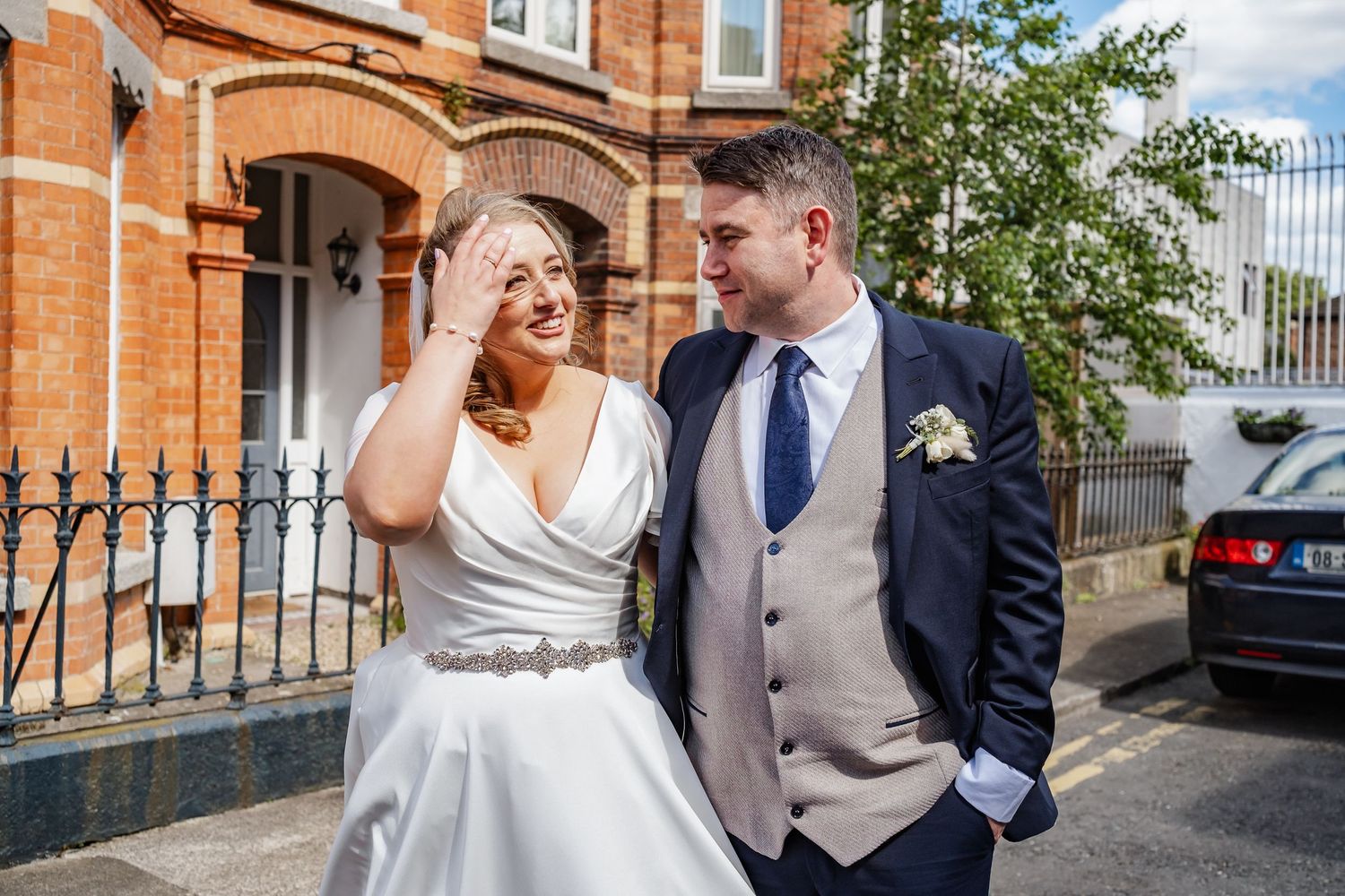 Candid moment of wedding couple laughing together outside brick building.
