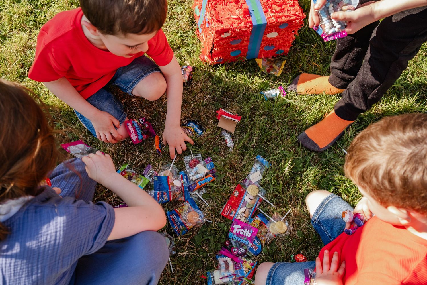 Children sitting in grass opening treats and candies during outdoor play.