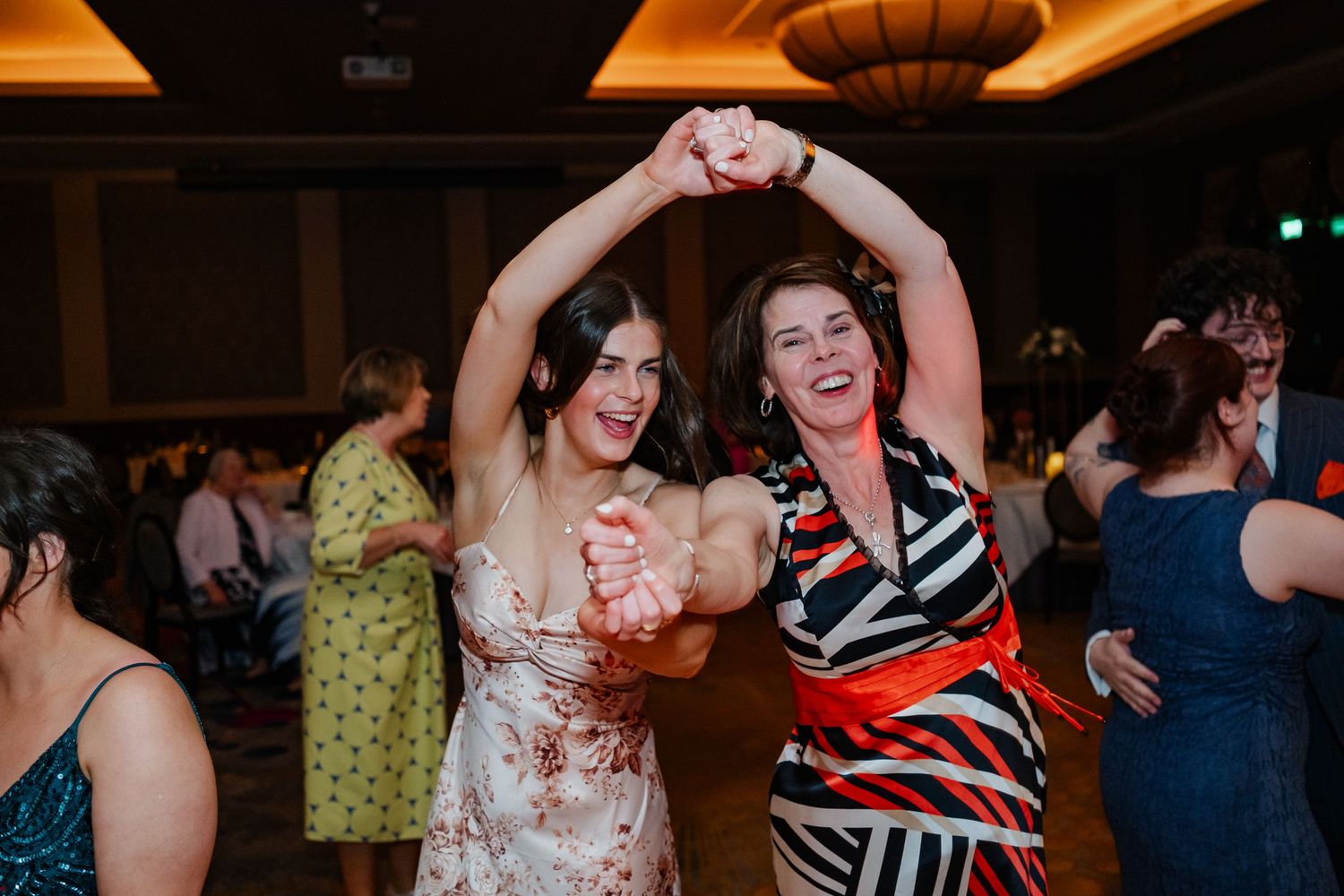 People dancing and socializing at a wedding reception with festive lighting and a lively dance floor atmosphere.