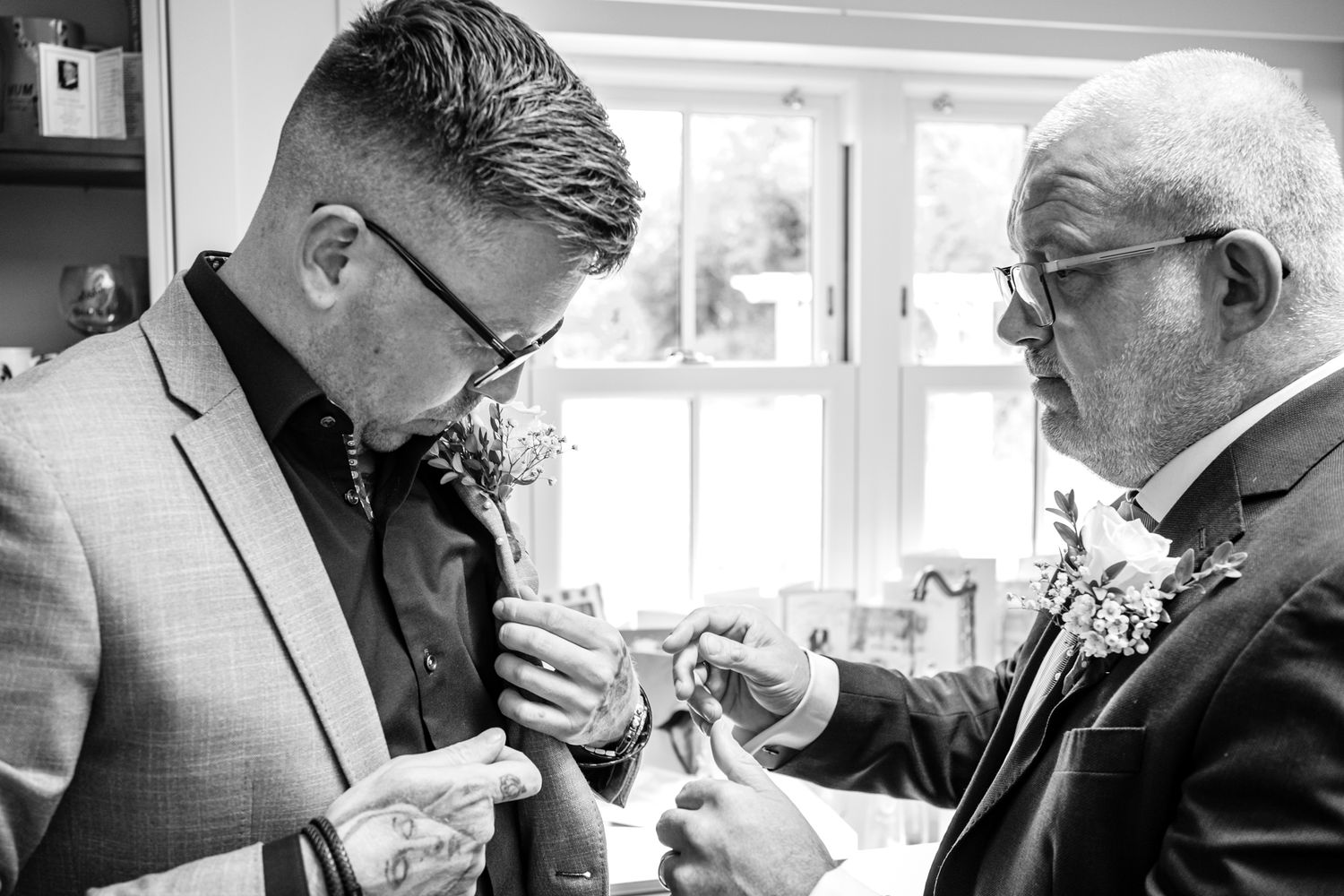Black and white image of men in formal wear pinning boutonnières.