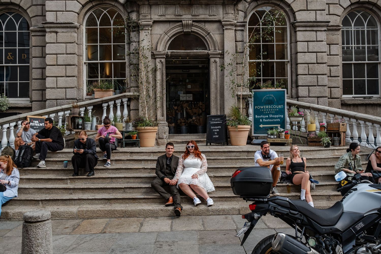Elegant historic building entrance with stone facade and arched windows where people relax on steps in urban setting.