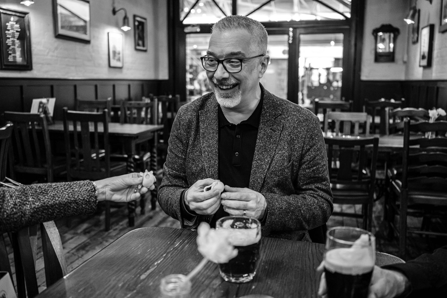 Person enjoying a pint of dark beer at a pub table.