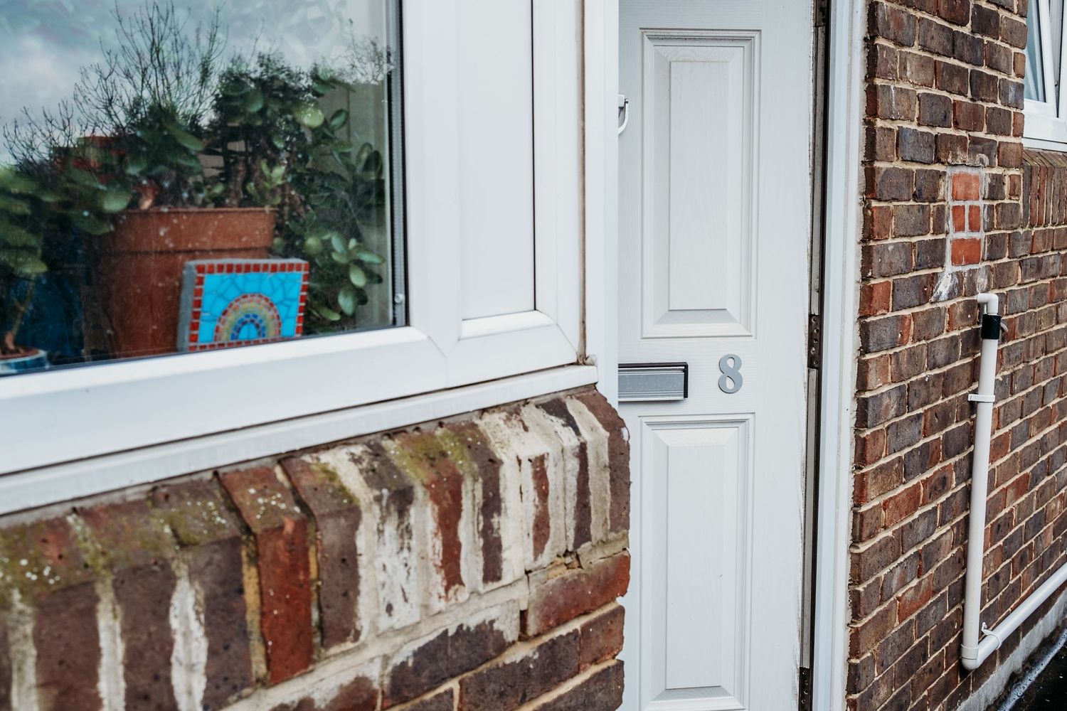 View through window showing potted plants and decorations on windowsill with brick wall background.