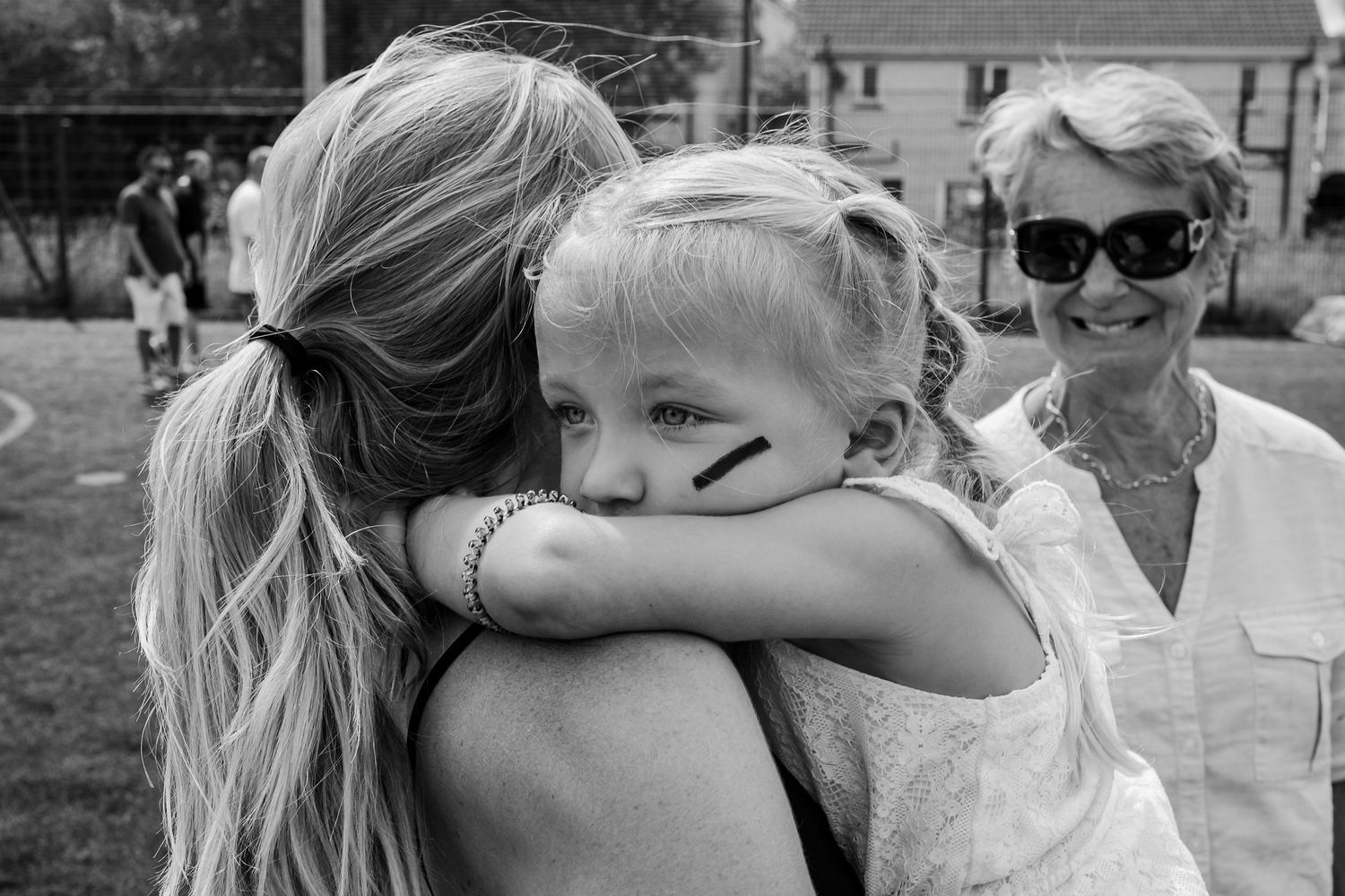 A heartfelt embrace shared outdoors on a sunny day with people in casual summer attire.