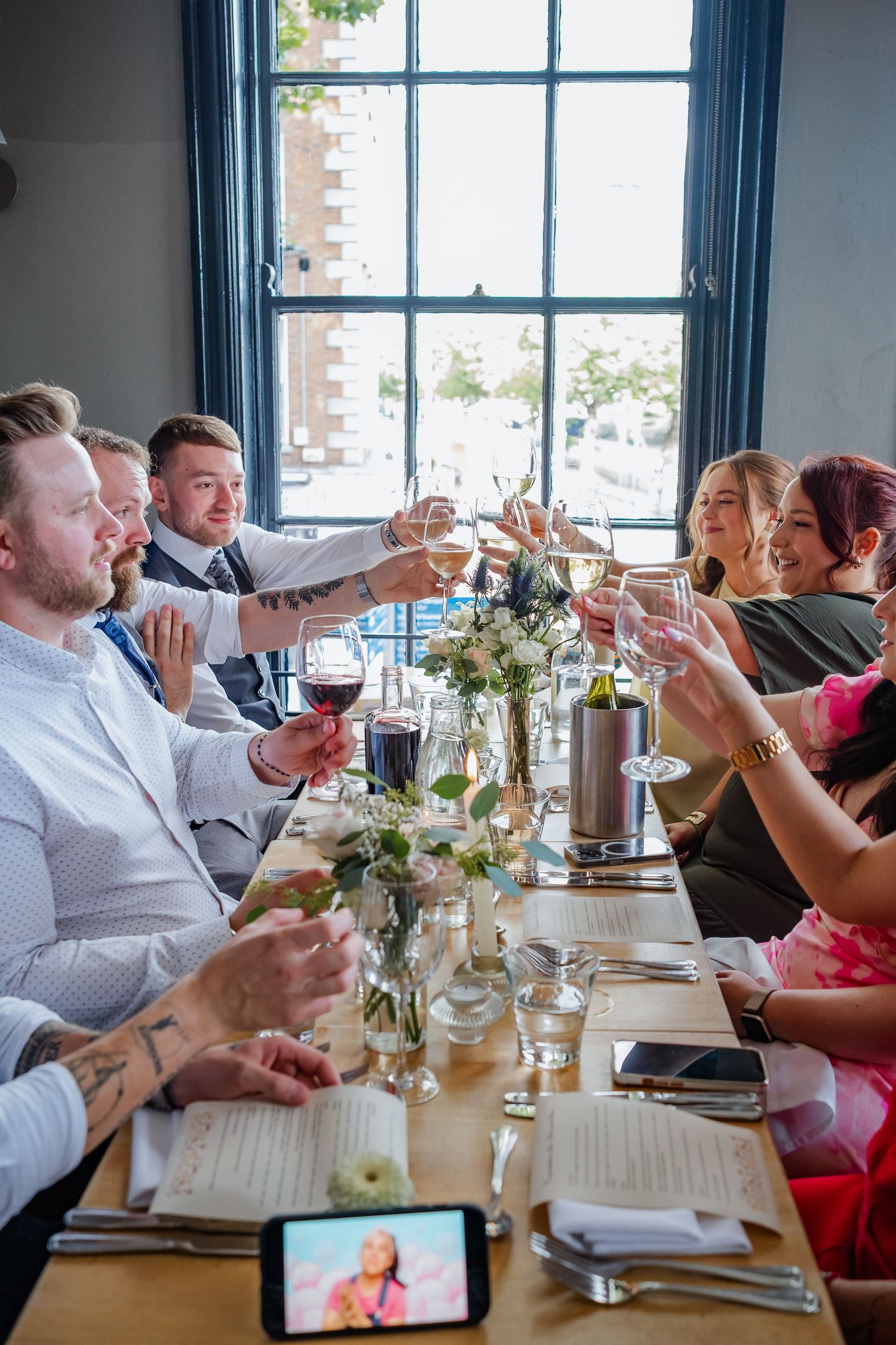 Wedding guests raise wine glasses in a toast during an elegant indoor reception dinner.