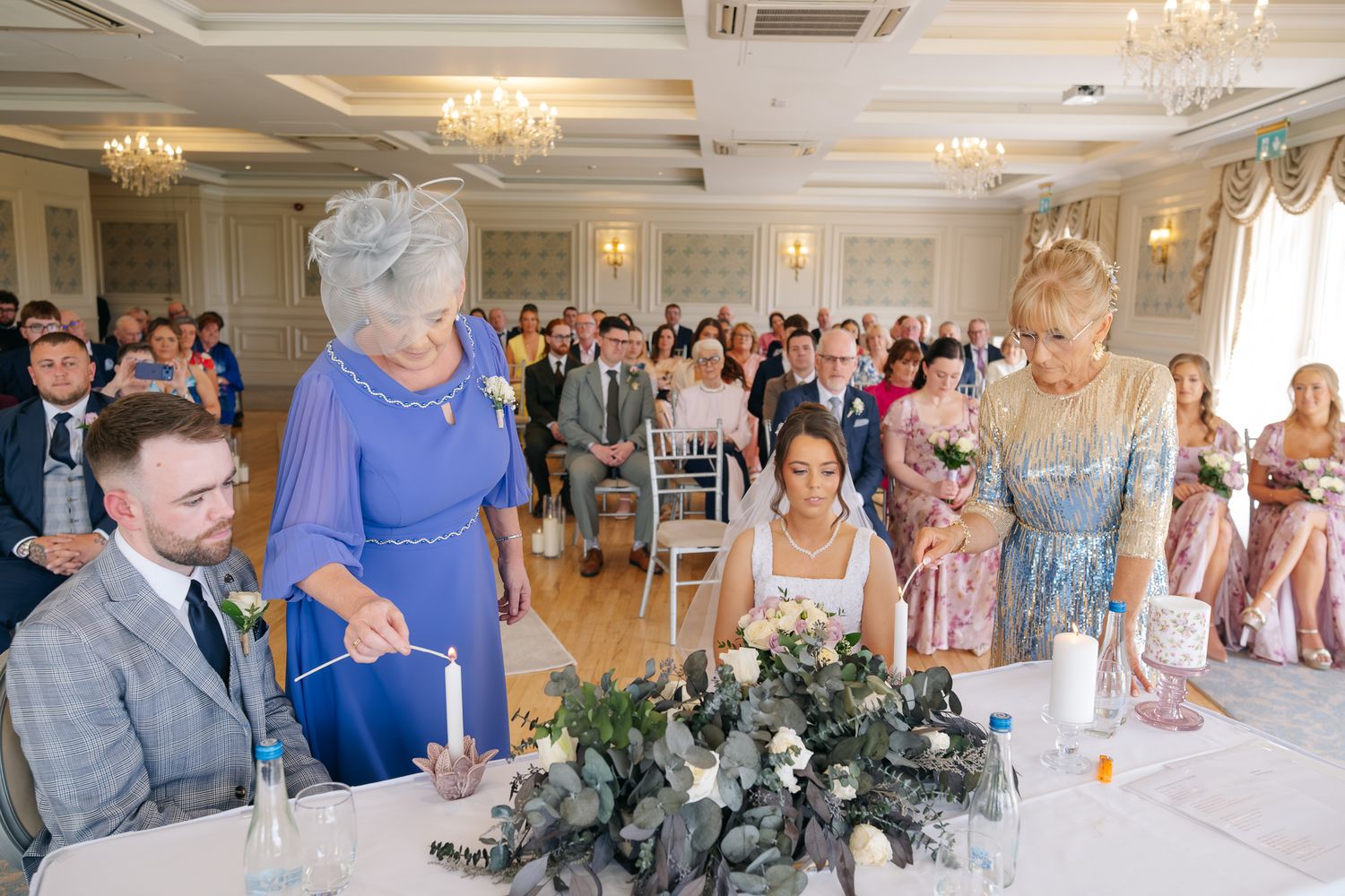 Elegant wedding ceremony with guests seated as family members light unity candle at decorated altar table.