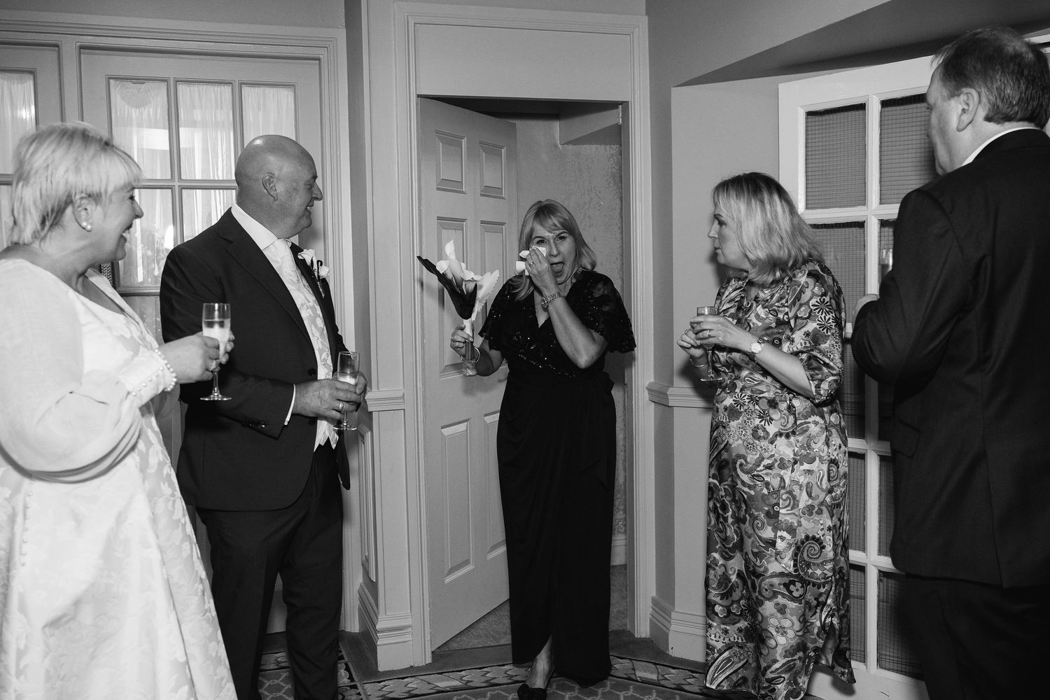 Black and white photo of elegantly dressed guests socializing at a formal wedding reception indoors.
