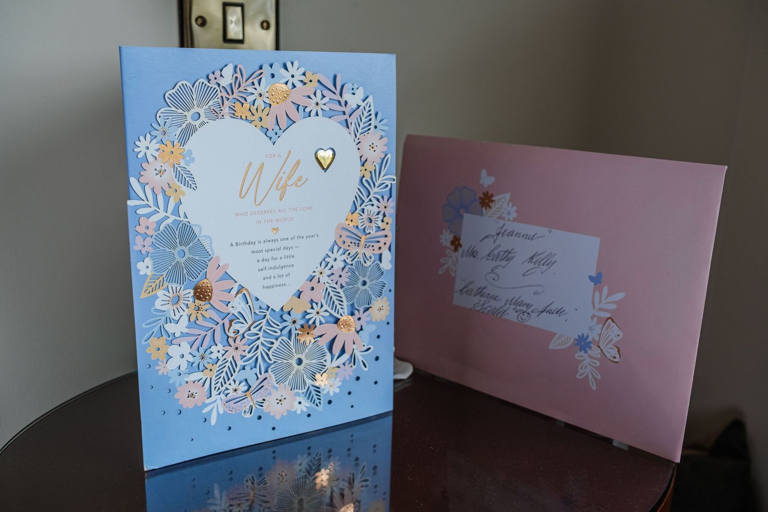 Elegant wedding cards for a wife featuring floral heart design on blue card and pink envelope on wooden table.