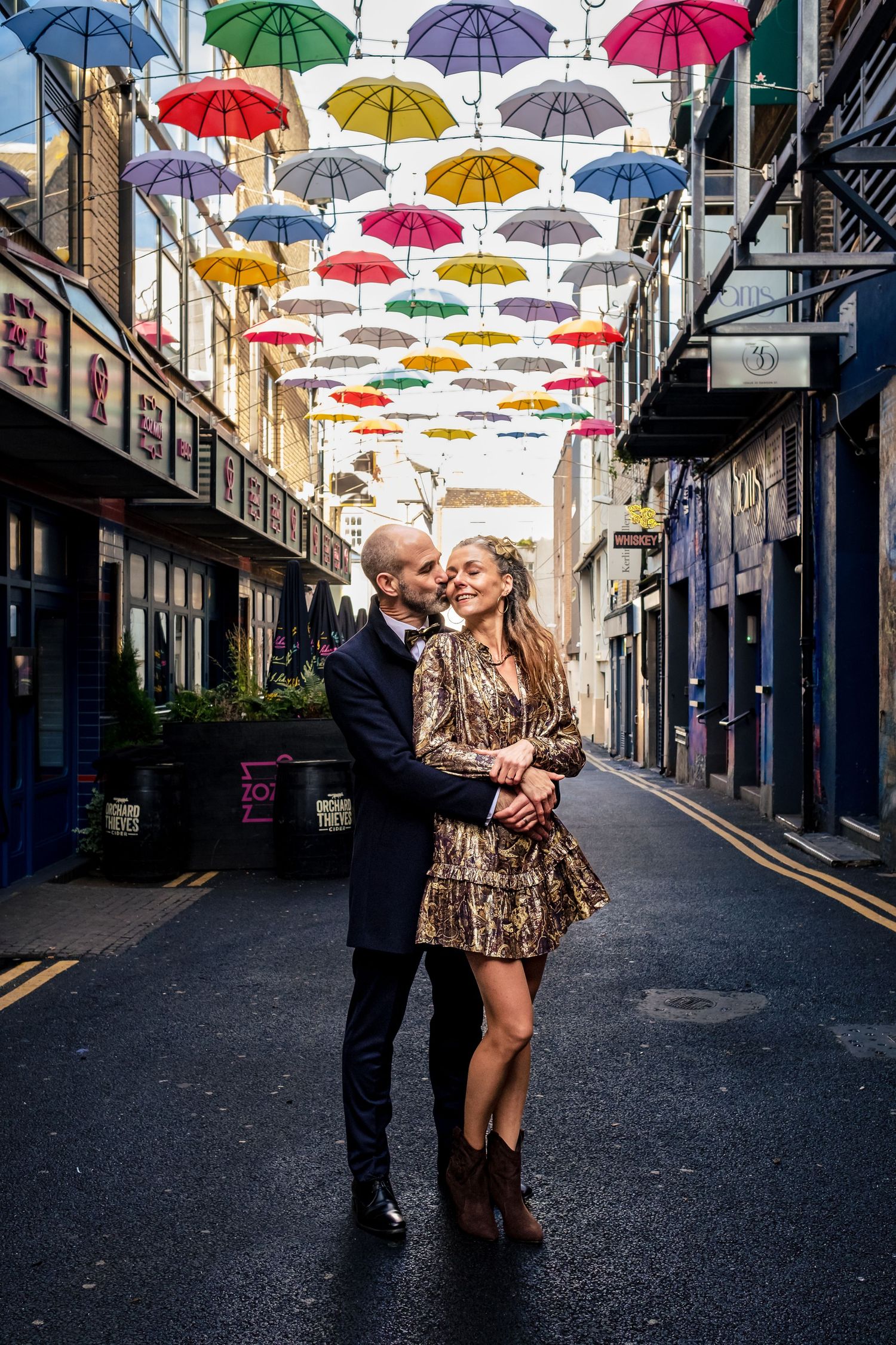 Couple embracing on street under colorful umbrella installation in urban alley.