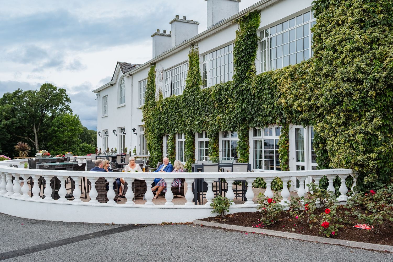 Elegant ivy-covered wedding venue exterior with white balustrade terrace and rose garden.