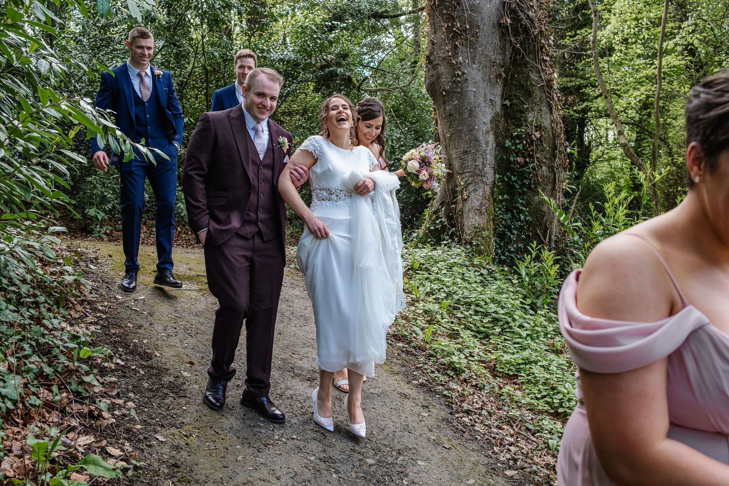 Wedding party walking through a scenic forest path surrounded by lush greenery.