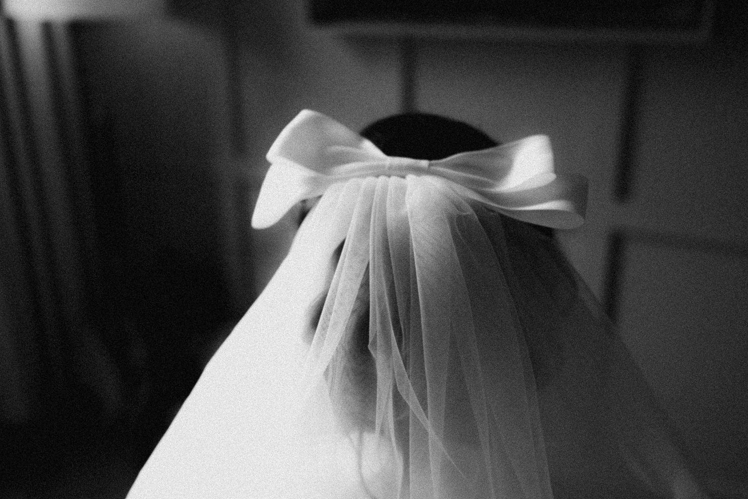 White wedding dress with tulle details captured from behind in dramatic black and white lighting.