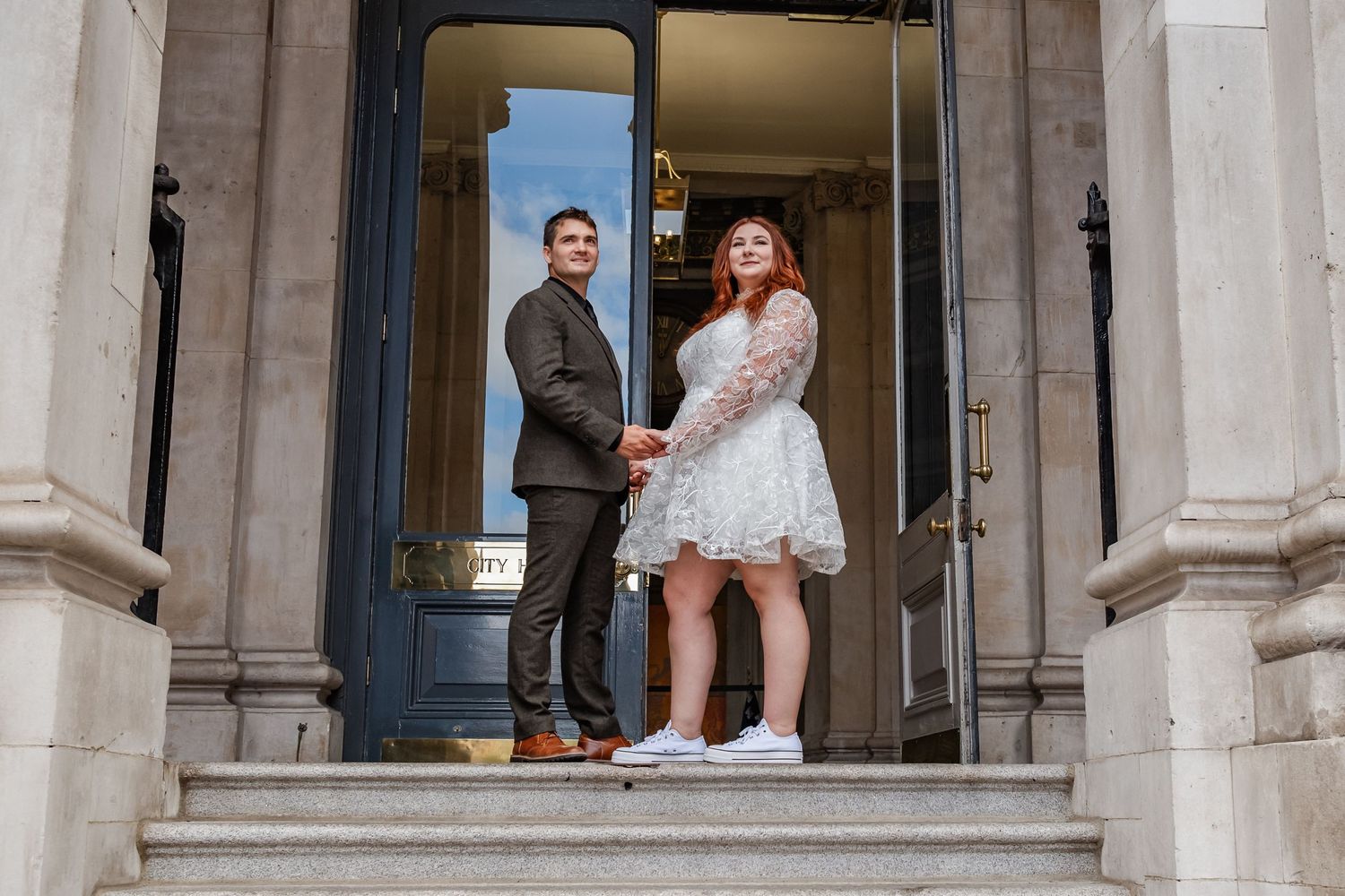 Couple posing in formal doorway entrance wearing casual wedding attire.