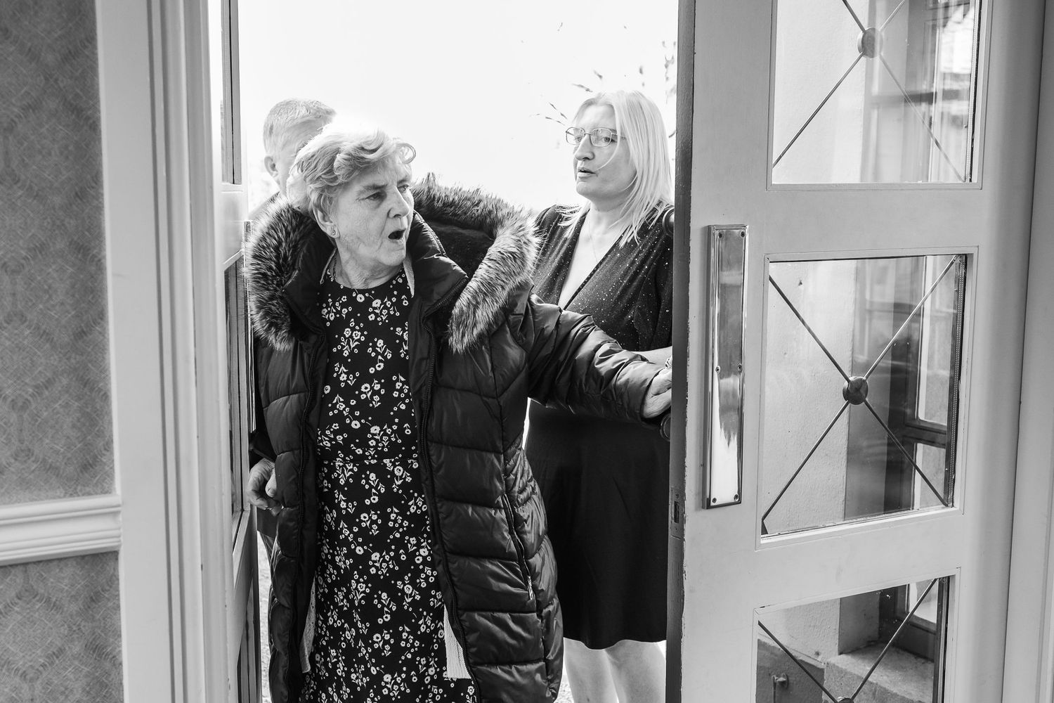 Black and white candid moment of wedding preparation through doorway.