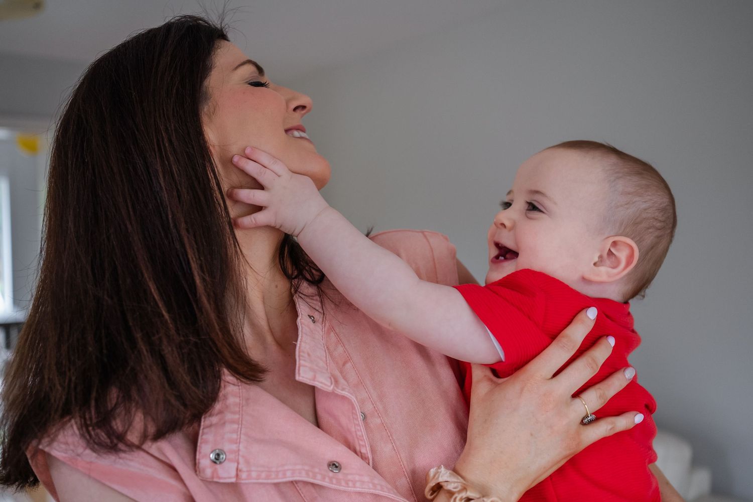 A joyful moment between parent and baby wearing red as they play and laugh together.