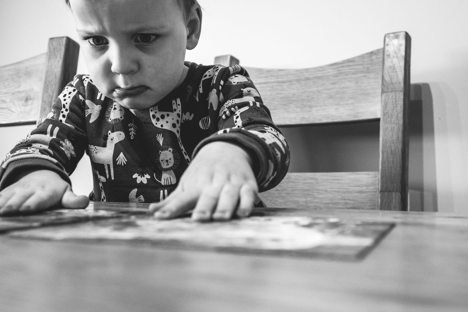 Close-up black and white image of a child looking down at a surface while sitting at a table.