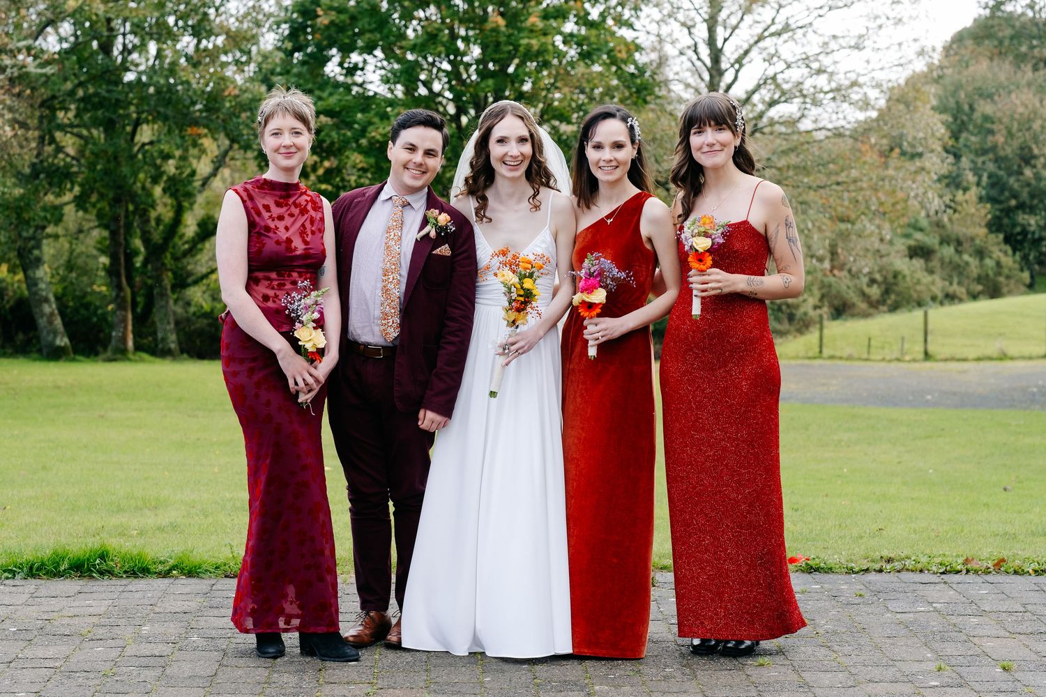 Wedding party poses outdoors in burgundy and white formal attire on a grassy lawn.