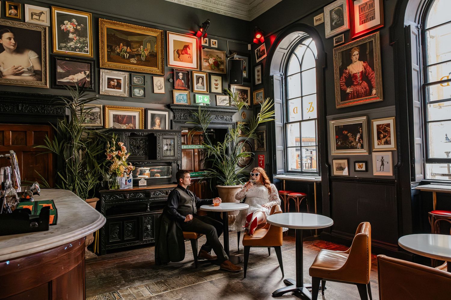 Vintage pub interior with gallery wall featuring wooden furniture and arched windows.