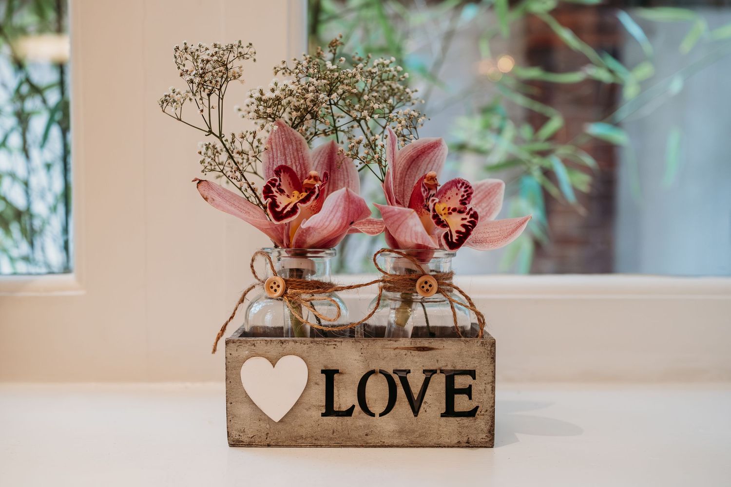 Pink flowers in mason jars inside a rustic wooden box with 'LOVE' text.