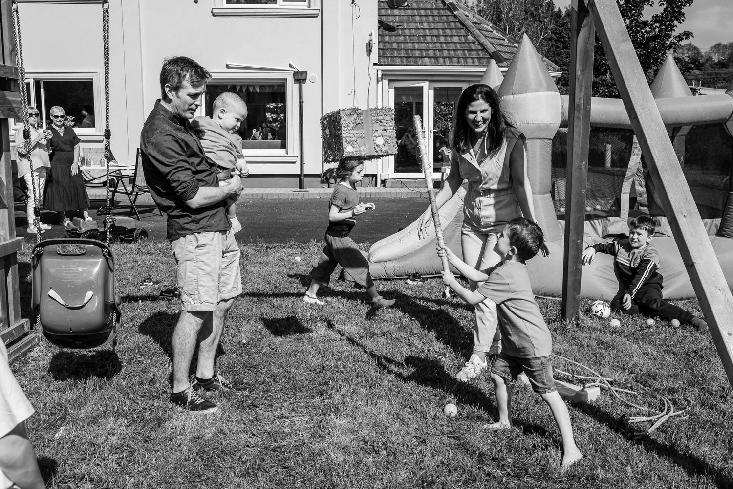 Black and white photo of families playing at an outdoor playground with swings.