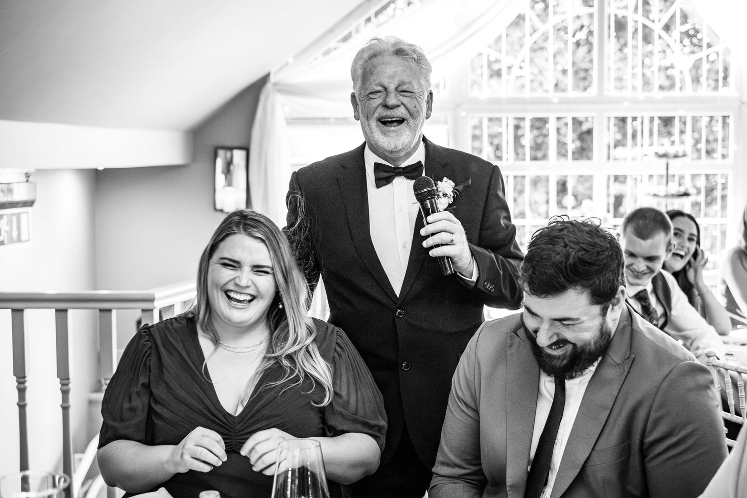 A candid black and white reception moment capturing laughter and joy during wedding speeches.