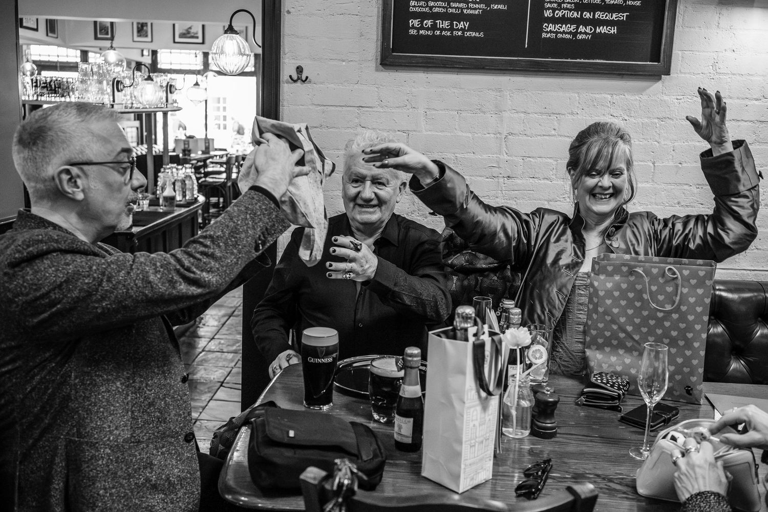 Group celebrating with raised glasses at casual gathering in monochrome.
