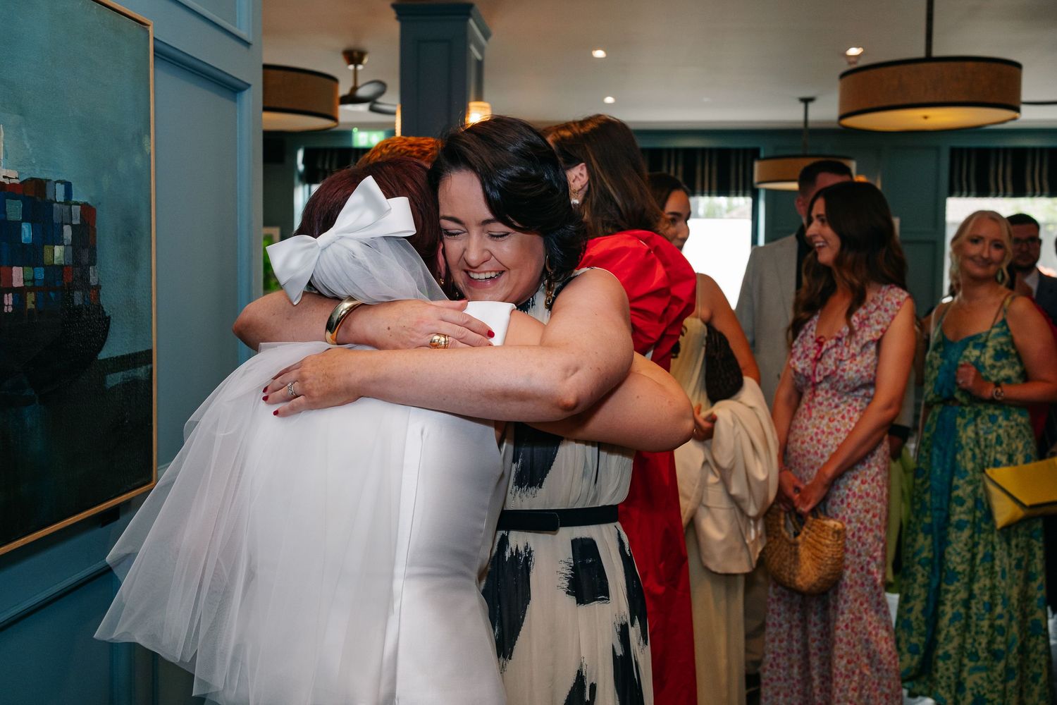 Emotional embrace during wedding celebration with guests looking on in background.