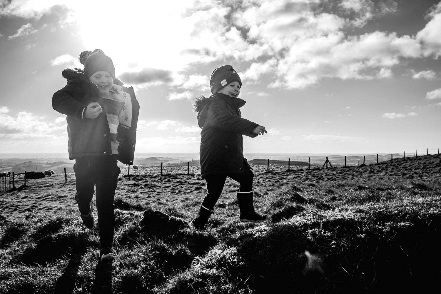 Silhouettes leaping on a hill with dramatic backlit sky and fence in background.
