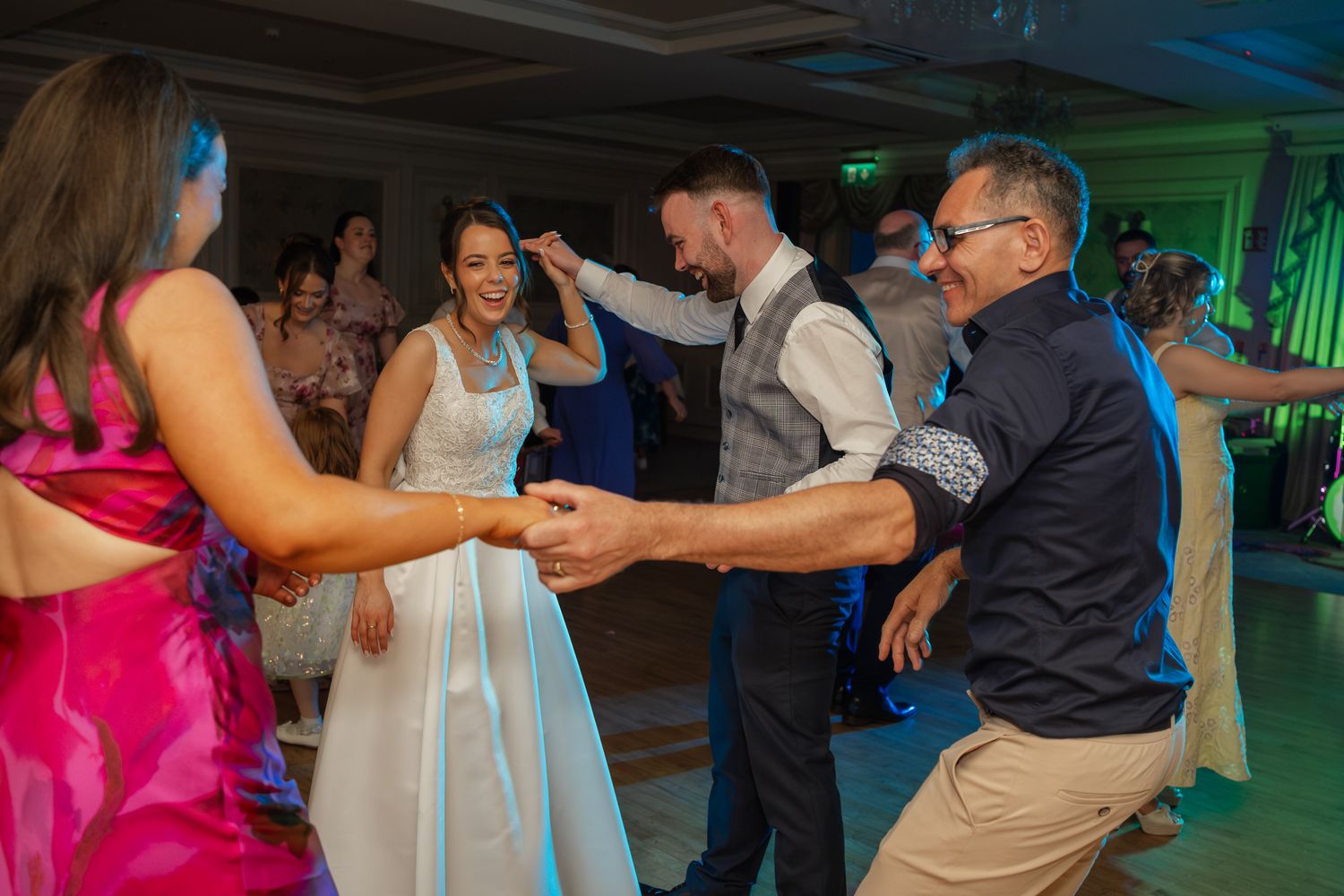 Bride and groom dancing joyfully with guests at a lively wedding reception on the dance floor.
