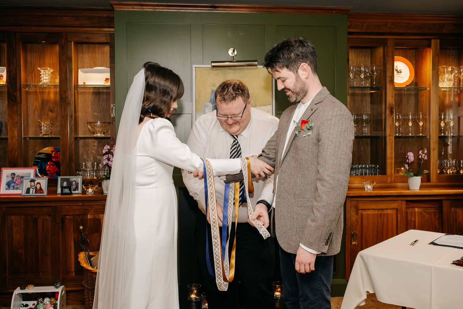 Couple exchanging handfasting vows with officiant during intimate indoor wedding ceremony.