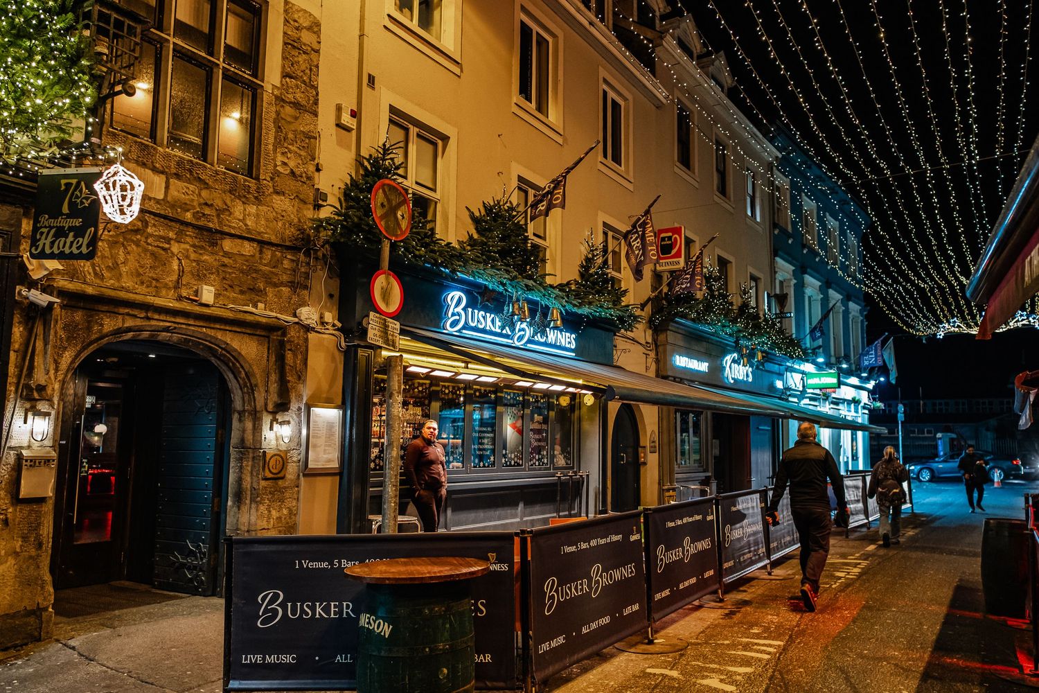 Bustling nighttime street scene outside Buskers Bar adorned with festive lights in Galway, Ireland.