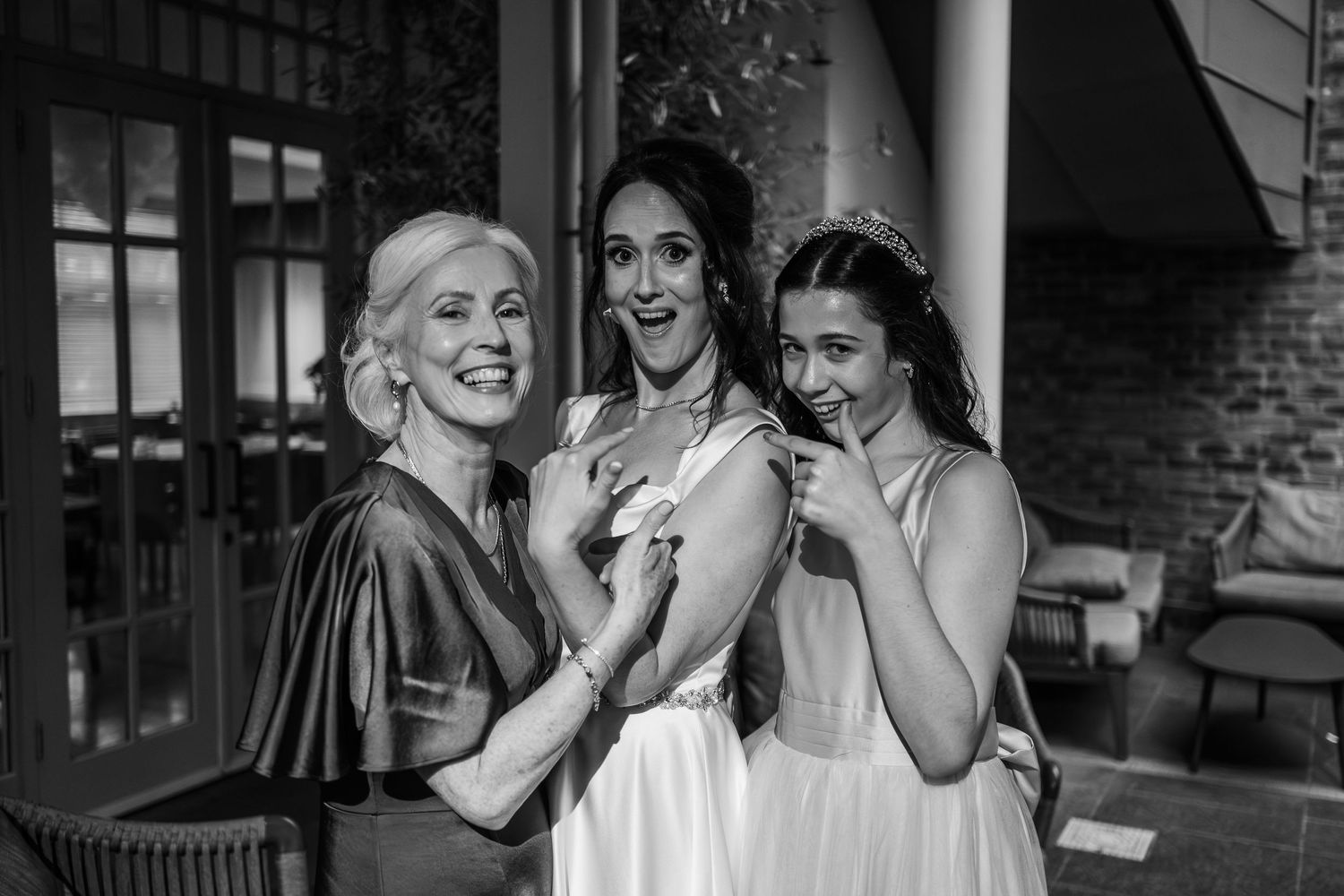 Three women share joyful laughter together on a porch in an elegant black and white wedding moment.