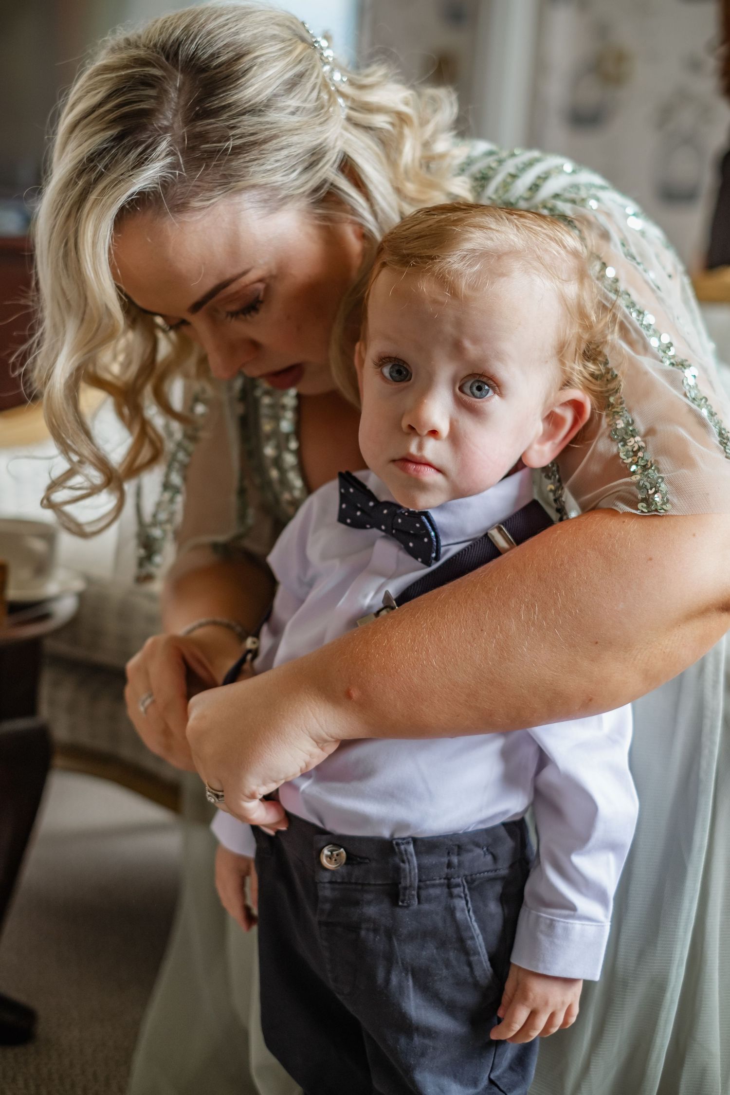 A young child in formal attire being held during wedding preparations.