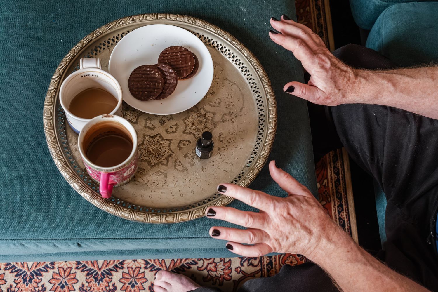 Two cups of tea and chocolate cookies served on an ornate metal tray.